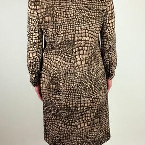 May include: A brown and beige dress with a crocodile print pattern. The dress has long sleeves and a knee-length skirt. The model is wearing black heeled shoes.