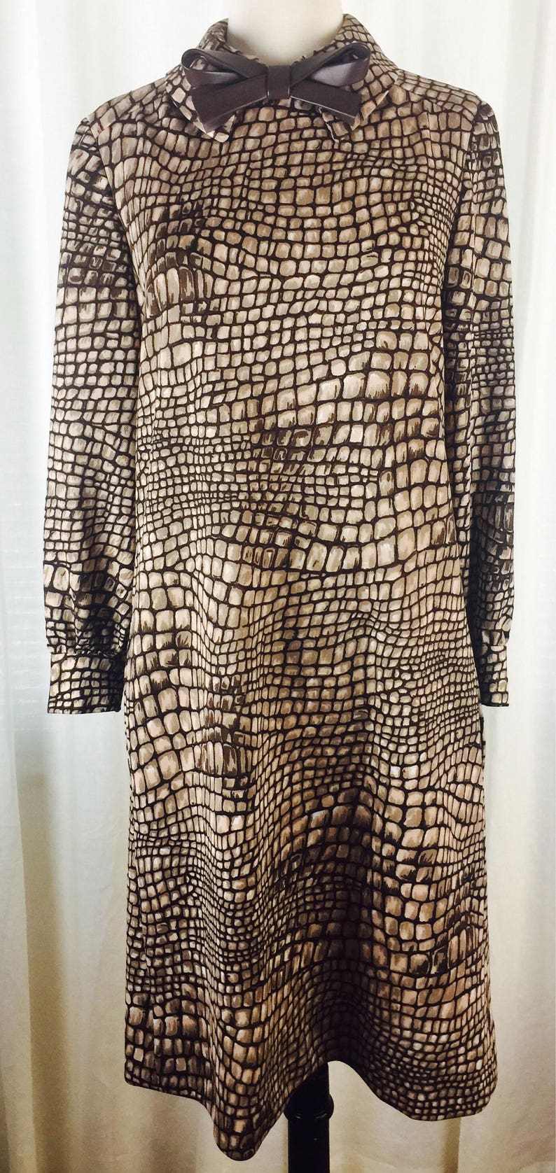 May include: A brown and beige dress with a snakeskin pattern. The dress has a collared neckline and a bow at the collar.
