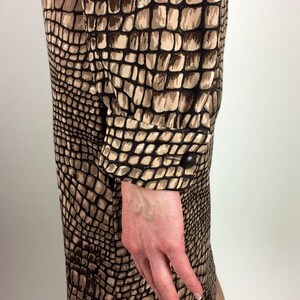 May include: A brown and beige dress with a crocodile print pattern. The dress has long sleeves with button cuffs.
