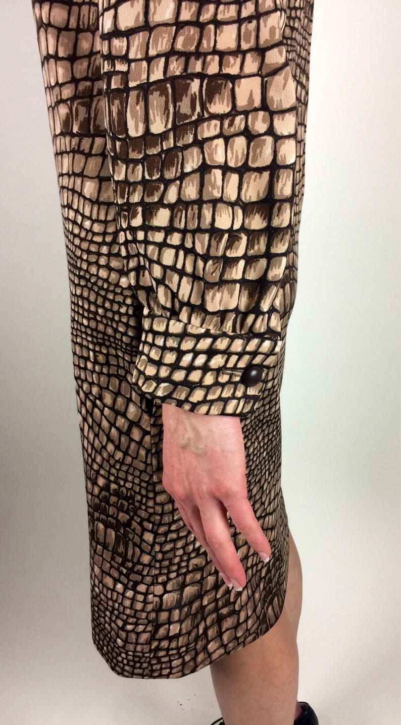 May include: A brown and beige dress with a crocodile print pattern. The dress has long sleeves with button cuffs.