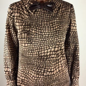 May include: A brown and beige dress with a crocodile print pattern. The dress has a long sleeve and a bow at the collar.