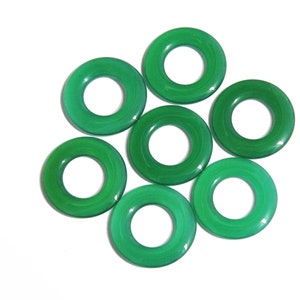Puede incluir: Siete piedras preciosas verdes circulares pulidas dispuestas en un patrón floral sobre un fondo blanco. Cada piedra tiene un agujero en el centro, creando una forma de rosquilla. Las piedras preciosas son de un color verde vibrante y sólido.