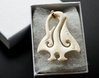 May include: A white bone carving of a traditional Maori design, with intricate details, in a white box with white cotton lining.