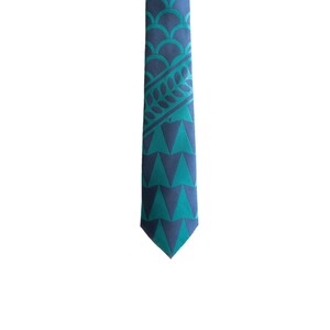 May include: A blue and green patterned silk tie with a geometric design. The tie has a pointed tip and is made of a smooth, luxurious fabric.