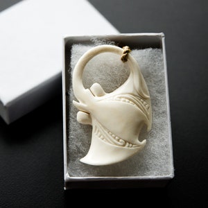 Op de afbeelding: Een wit bottenbeeldje van een mantarog met ingewikkelde details, gepresenteerd in een witte doos met wit tissuepapier.