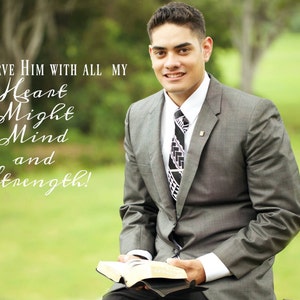 May include: A man in a gray suit and a patterned tie is holding a book. The text on the book reads "I will serve Him with all my Heart Might Mind and Strength!"