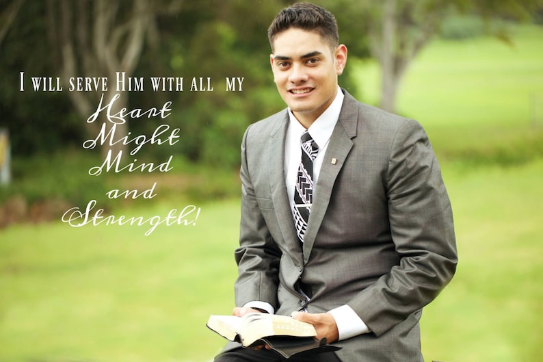 May include: A man in a gray suit and a patterned tie is holding a book. The text on the book reads "I will serve Him with all my Heart Might Mind and Strength!"