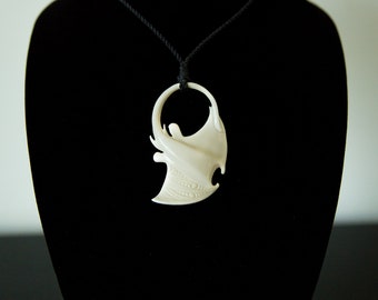 May include: A white bone pendant carved in the shape of a manta ray, hanging from a black cord on a black velvet display stand.
