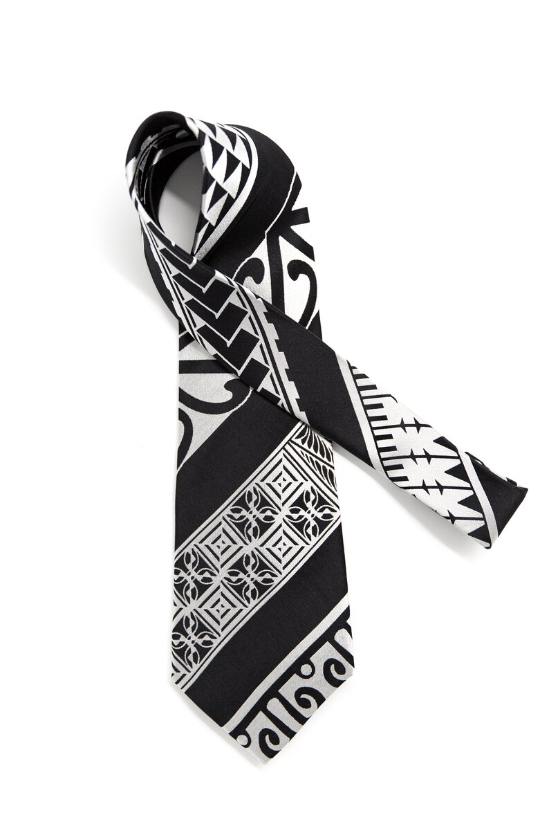 May include: A black and white patterned tie with a geometric design. The tie is made of a silky material and has a pointed end.
