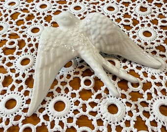 May include: A white ceramic bird figurine with outstretched wings and detailed feather textures. The bird is depicted in a flying position with its head turned slightly to the side, featuring a smooth, glossy finish across its entire surface.