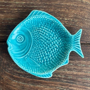 Pode incluir: Um prato de cerâmica em forma de peixe azul turquesa com uma superfície texturizada. O prato é perfeito para servir petiscos ou pratos pequenos.
