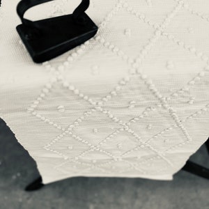 May include: A black iron with a handle on a white fabric with a textured pattern.
