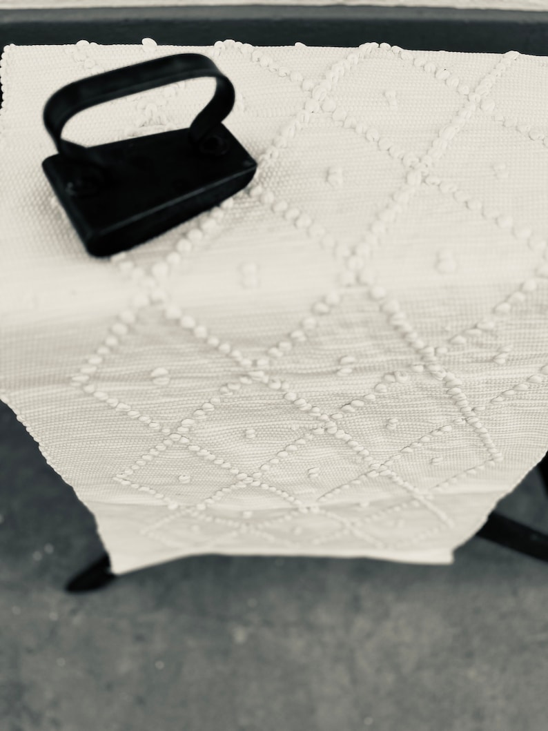 May include: A black iron with a handle on a white fabric with a textured pattern.
