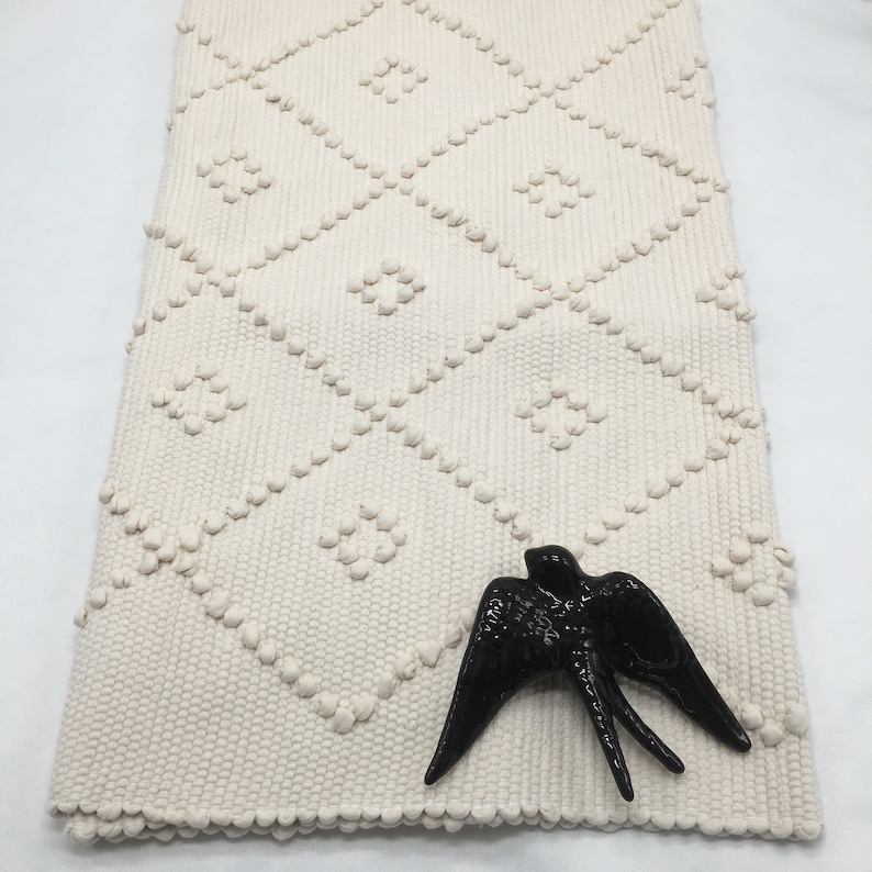 May include: A white woven rug with a diamond pattern and a black ceramic swallow figurine on top.