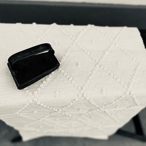 May include: A black iron with a handle on a white textured rug with a diamond pattern.