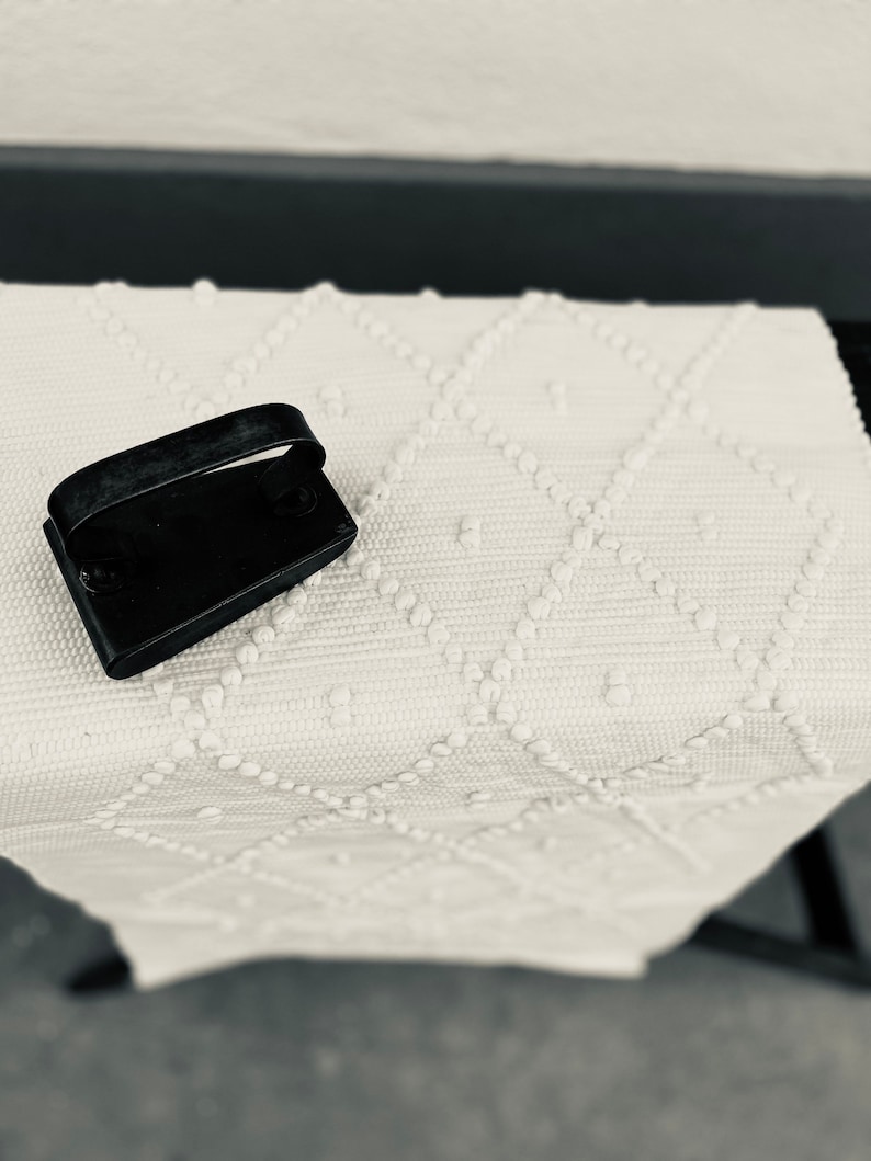 May include: A black iron with a handle on a white textured rug with a diamond pattern.