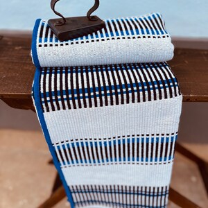 May include: A white and blue striped fabric with black stripes, folded in half and sitting on a wooden surface. An old iron sits on top of the fabric.