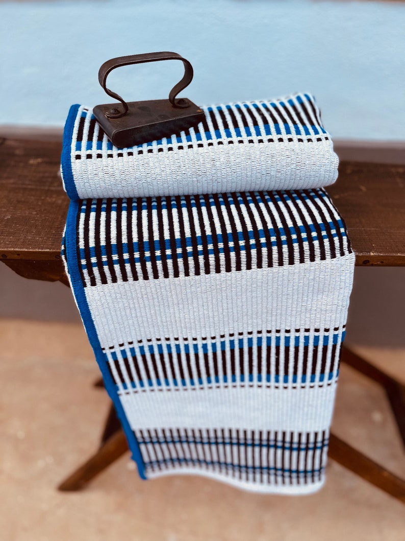 May include: A white and blue striped fabric with black stripes, folded in half and sitting on a wooden surface. An old iron sits on top of the fabric.