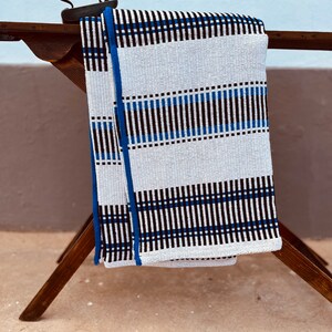 May include: A white and blue striped throw blanket with black accents. The blanket is folded and draped over a wooden ironing board.