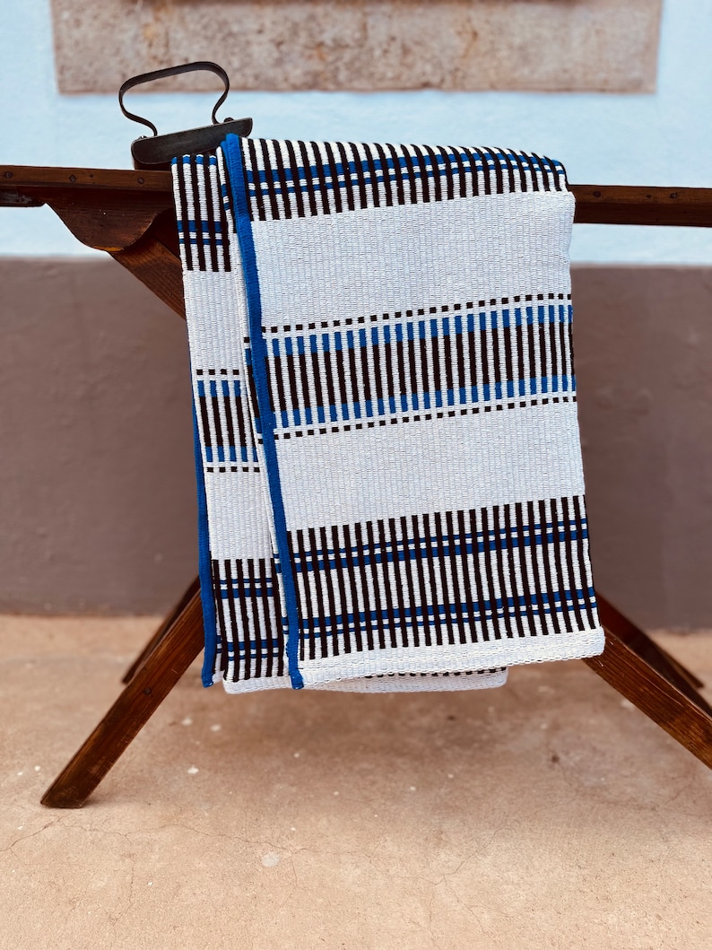 May include: A white and blue striped throw blanket with black accents. The blanket is folded and draped over a wooden ironing board.