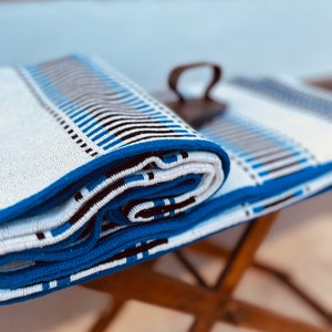 May include: A white and blue striped throw blanket is rolled up and placed on a wooden table. The blanket has a blue border and black stripes.