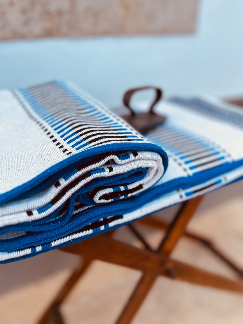 May include: A white and blue striped throw blanket is rolled up and placed on a wooden table. The blanket has a blue border and black stripes.