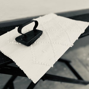May include: A vintage black iron with a handle on a white ironing board with a textured surface.