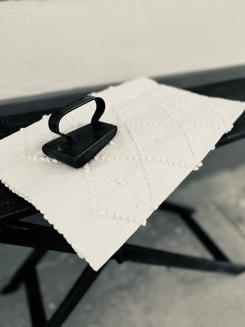 May include: A vintage black iron with a handle on a white ironing board with a textured surface.