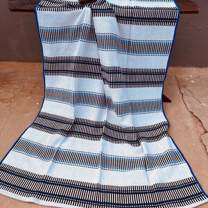 May include: A white and blue striped throw blanket with black stripes. The blanket is folded and draped over a wooden surface.