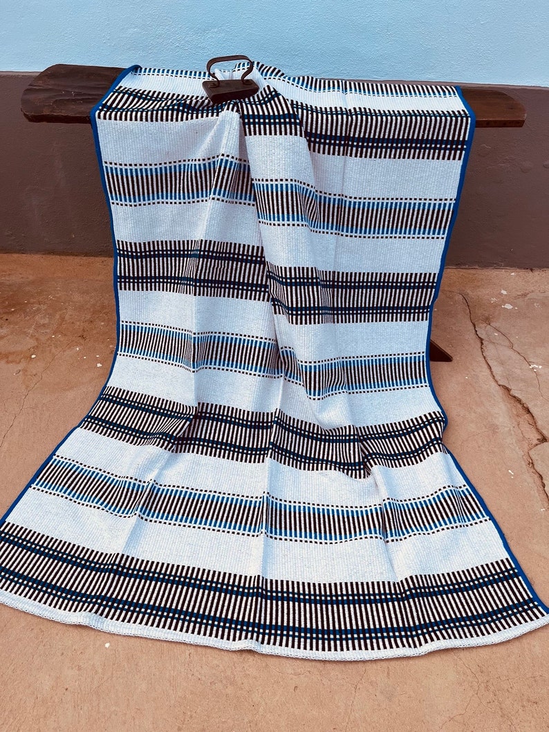 May include: A white and blue striped throw blanket with black stripes. The blanket is folded and draped over a wooden surface.