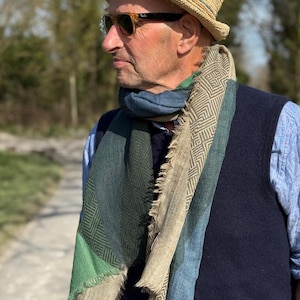 May include: A man wearing a straw hat, sunglasses, and a multi-colored scarf with a geometric pattern. The scarf is made of a soft, woven fabric and has a fringed edge.