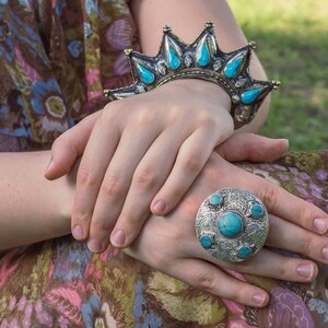 Könnte beinhalten: Eine Frau trägt ein Blumenkleid mit einer türkisfarbenen Anhängerkette und einem silbernen Armband mit türkisfarbenen Steinen. Sie trägt auch einen großen silbernen Ring mit türkisfarbenen Steinen.
