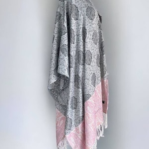 Könnte beinhalten: Ein grau-rosa gemustertes Kimono mit Fransenbesatz. Der Kimono hat ein florales Design mit einem Paisley-Muster am Saum.