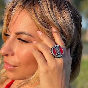May include: A silver ring with a red and turquoise stone inlay. The ring is round and has a decorative border.