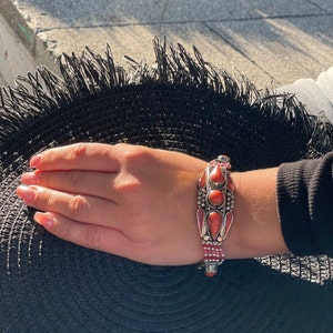 May include: A silver bracelet with red gemstone accents. The bracelet has a beaded design and a decorative centerpiece.