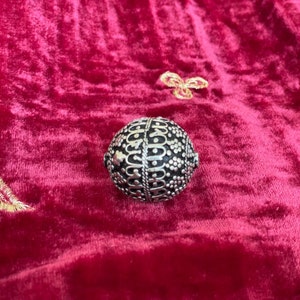 May include: A silver metal bead with an intricate geometric pattern. The bead is round and has a smooth surface.