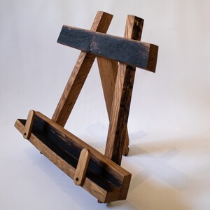 May include: A wooden easel made from reclaimed wood with a dark brown stain. The easel has a shelf for displaying items.