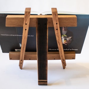 May include: A wooden book stand made from reclaimed oak barrel staves. The stand is holding a cookbook titled "Classic home cooking, by Britain's ...ative chef. Heston Blumenthal at home".