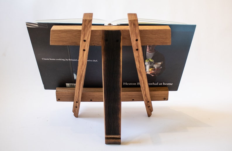 May include: A wooden book stand made from reclaimed oak barrel staves. The stand is holding a cookbook titled "Classic home cooking, by Britain's ...ative chef. Heston Blumenthal at home".