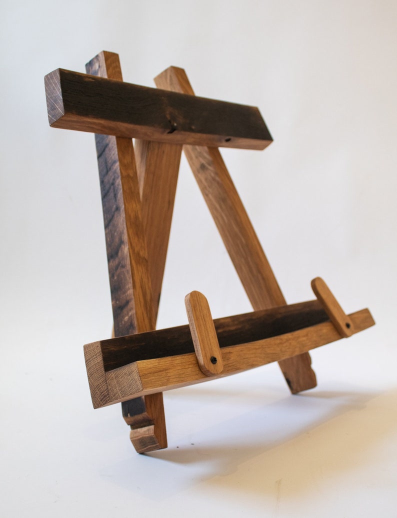May include: A wooden easel made from reclaimed wood with a dark brown stain. The easel has two adjustable supports and a small shelf for displaying items.