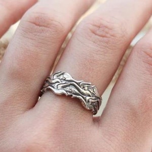 May include: A silver ring with a textured, organic design. The ring is worn on a person's finger.