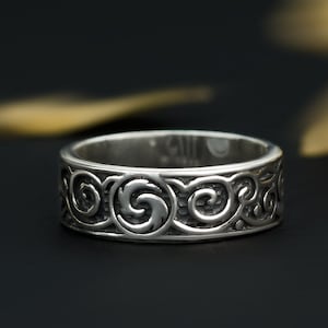 May include: A silver ring with a detailed swirling pattern. The ring is on a black background.