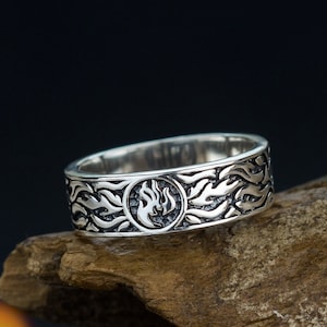 May include: A silver ring with a flame design. The ring is on a piece of wood.