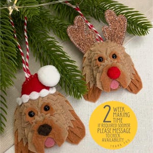 May include: Two felt Christmas ornaments shaped like a dog. One dog is wearing a Santa hat and the other has reindeer antlers. The ornaments are hanging from a Christmas tree branch. The text on the yellow circle reads: "2 week making time. If required sooner please message to check availability. Thank you."