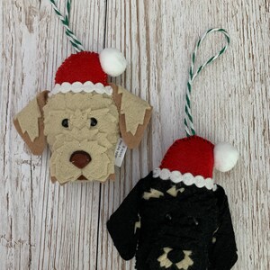 May include: Two felt Christmas ornaments, one is a dog wearing a Santa hat and the other is a dog wearing a black and white sweater with a Santa hat.