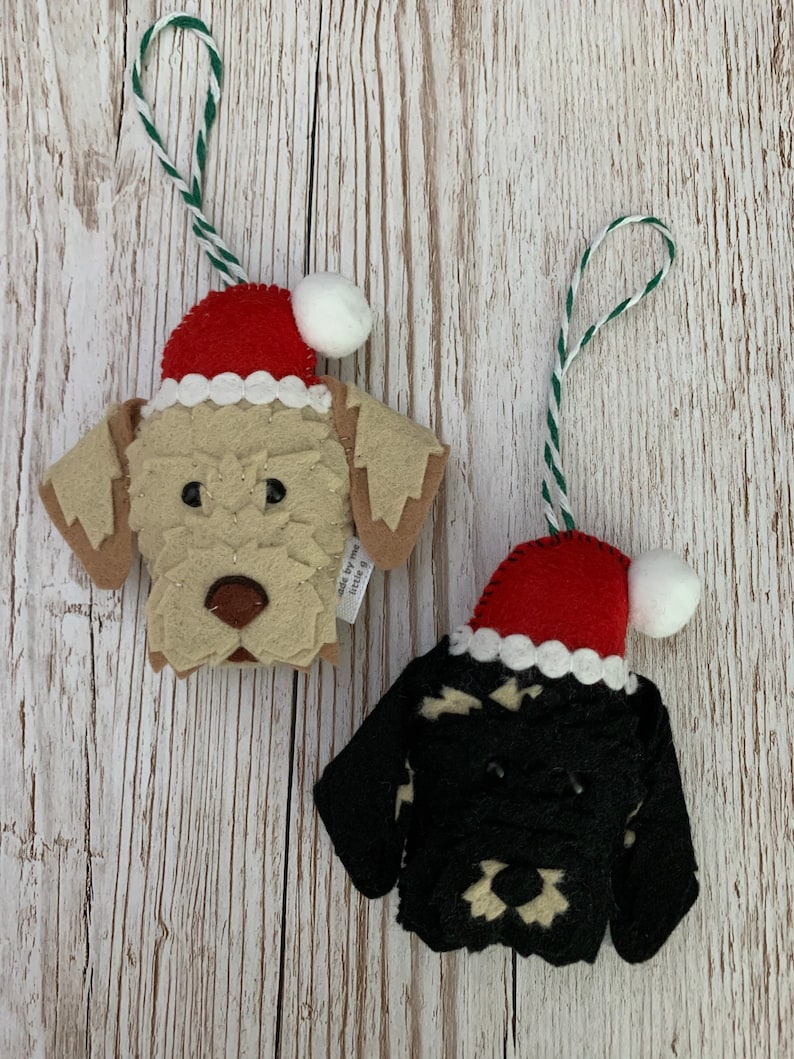 May include: Two felt Christmas ornaments, one is a dog wearing a Santa hat and the other is a dog wearing a black and white sweater with a Santa hat.