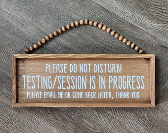 May include: A wooden sign with the text "PLEASE DO NOT DISTURB! TESTING/SESSION IS IN PROGRESS PLEASE EMAIL ME OR COME BACK LATER, THANK YOU" in white lettering. The sign is hanging from a string of wooden beads.