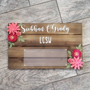 May include: Wooden sign with the name Siobhan O'Grady and the letters LCSW. The sign is decorated with pink paper flowers.