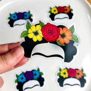 May include: Five clear stickers with black outlines of a woman's face with a flower crown. The flowers are red, yellow, orange, and purple. The stickers are on a white surface.