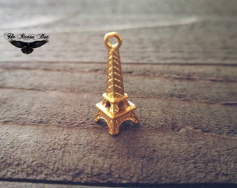 May include: A gold-colored Eiffel Tower charm pendant. The charm is small and detailed, with a textured surface.